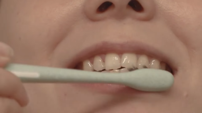 A Person Is Brushing Their Teeth with A Green Toothbrush, Focusing on The Front Upper Teeth to Maintain Oral Hygiene