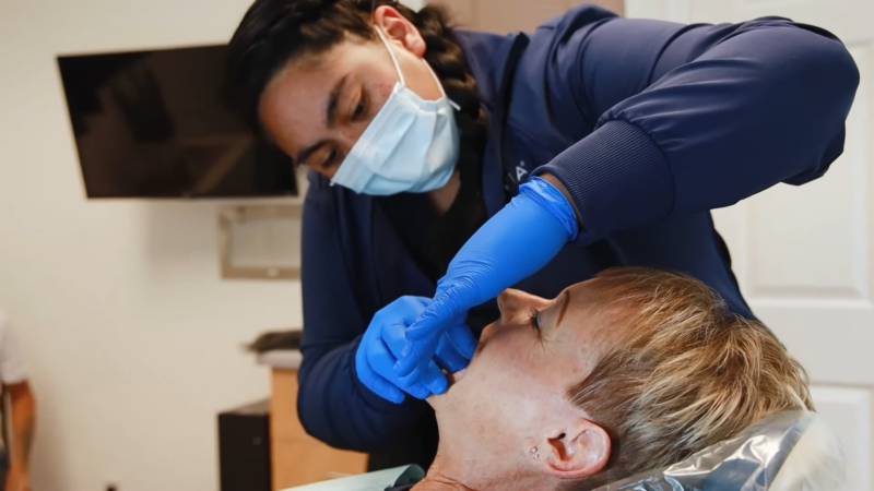 A Dental Professional Wearing a Mask and Gloves Performs a Dental Examination on A Patient Lying Back in A Dental Chair