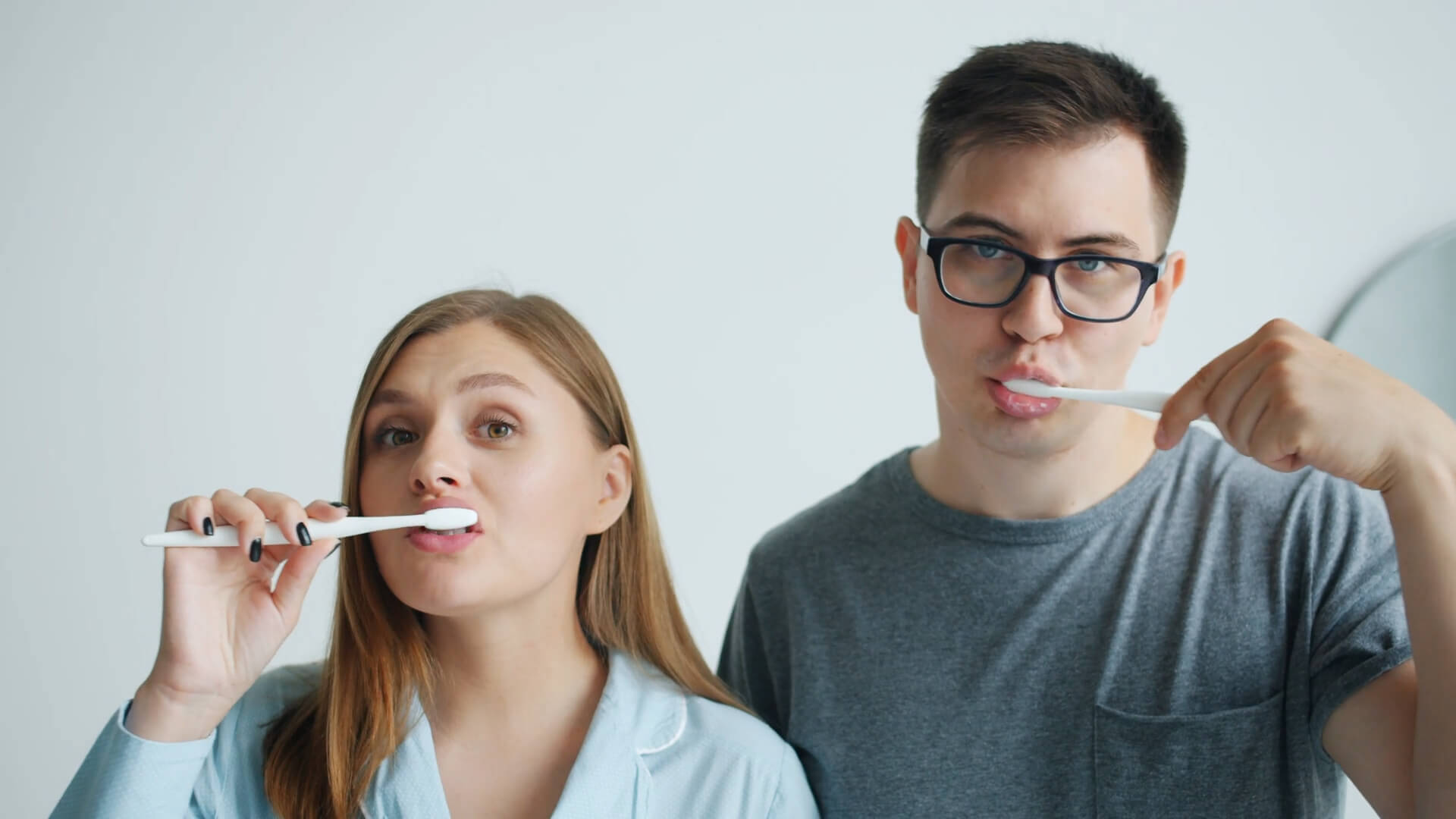 The guy and the girl are brushing their teeth in the morning